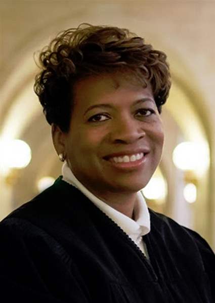 A headshot of Justice Melody J. Stewart in a well-lit hallway. Justice Stewart is a Black woman with short brown hair, wearing a white shirt under a black judicial robe.