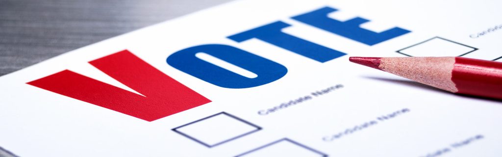 A blank ballot with red and blue font lays under a red pencil.