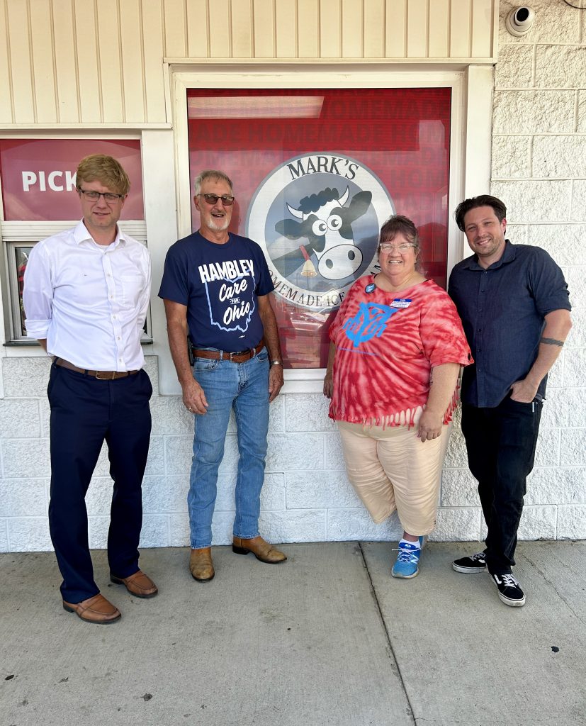 Bryan Hambley, Allen Laferty, Alena Fox, and Chris Volpe Stand in front of Mark's Homemade Ice Cream cartoonish cow logo Largely framed in a window.