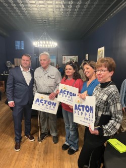 Mary Beth stands in the middle of a row of 5 men and women holding Acton/Pepper signs and smiling optimistically.